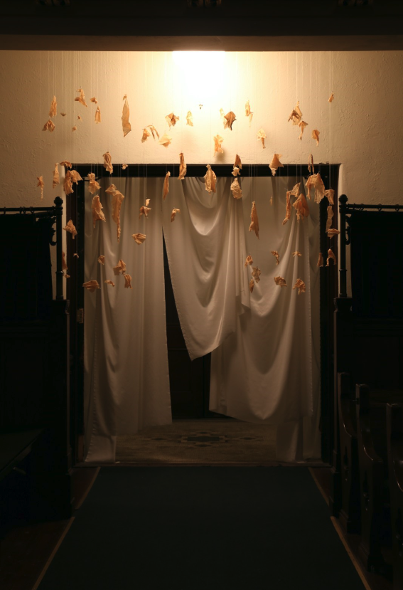A door frame draped with fabric. Additional pieces of fabric are suspended over the doorway by thin, translucent string.
